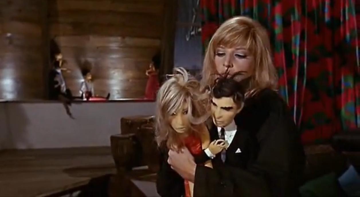 Figure 36: Modesty Blasie (Monica Vitti) holds dolls of herself and Paul Hagan (Michael Craig) in Losey’s Modesty Blaise, 1966. More dolls line the wall.